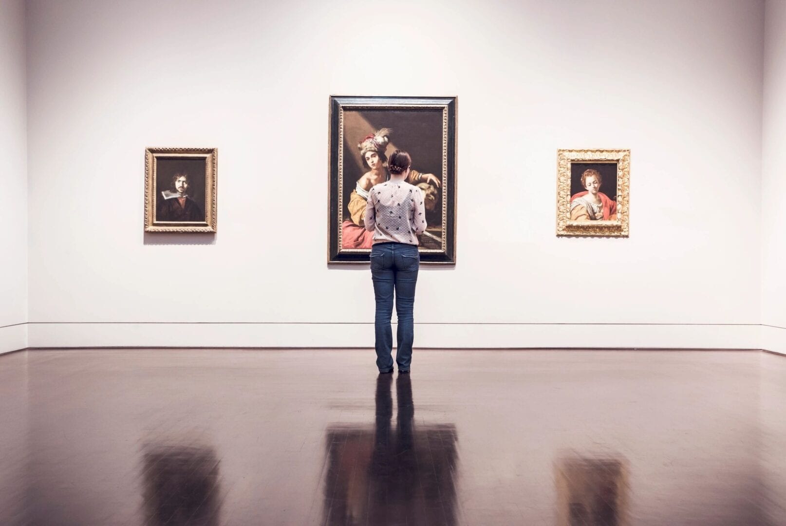 Person observing paintings in an art gallery with polished floors.
